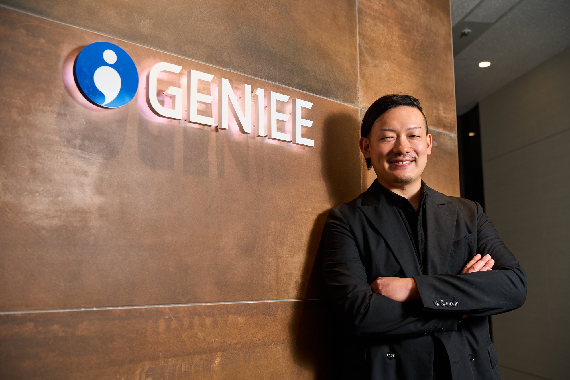 GENIEEのロゴが入った壁の前に立つ長島崇斗氏