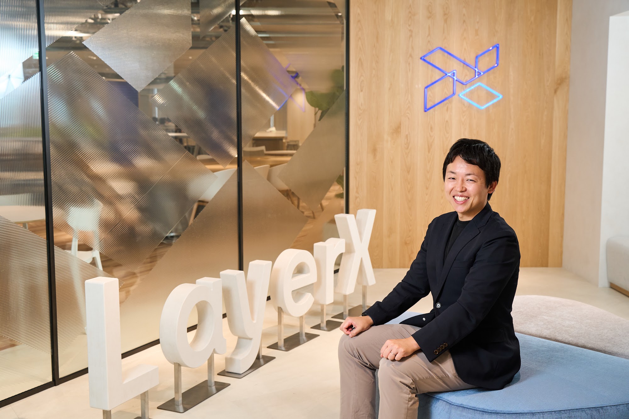 LayerXのロゴの前に立つ清水敬大氏