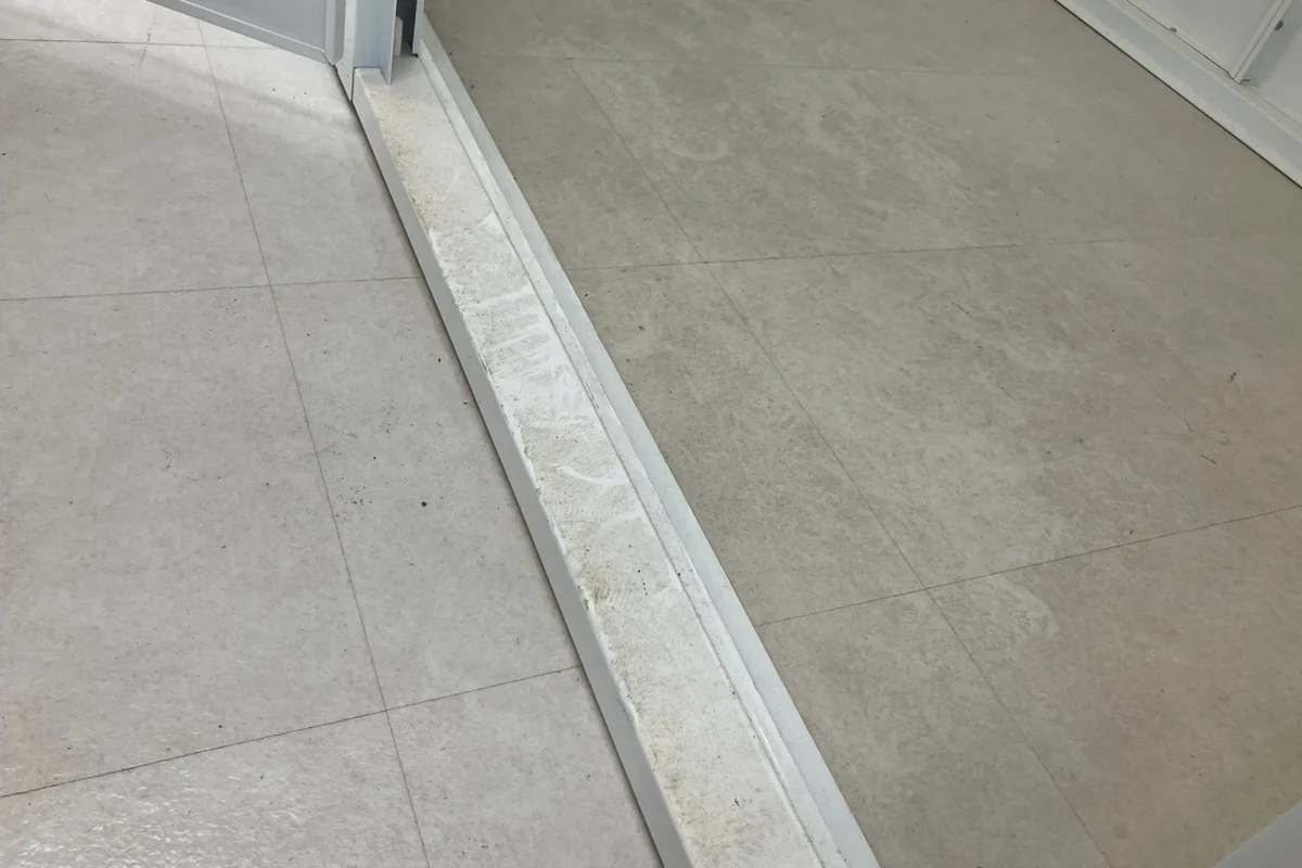 清掃前：扉の敷居レールに砂ぼこりと汚れが溜まった状態